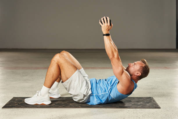 istock a young Caucasian athlete pumps his abs while lying on the floor with his knees bent, pushing his arms up with weights. fitness. aerobics. exercises on the mat. physical health 1904493892