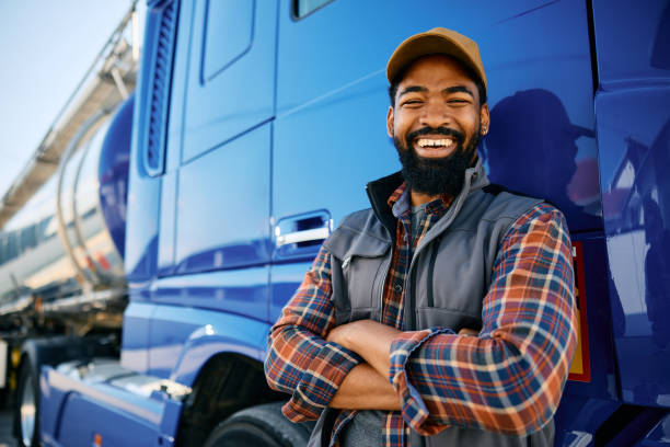 istock Cheerful black truck driver leaning on his vehicle and looking at camera. 1904500540