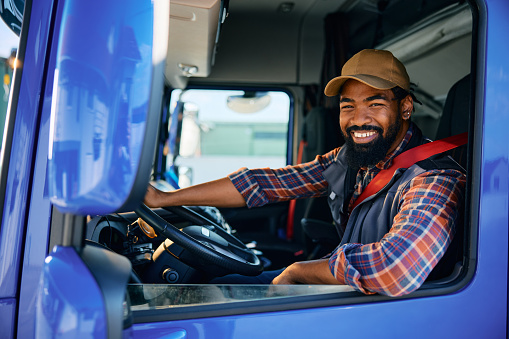 Happy African American professional driver sitting in truck cabin and looking at camera.