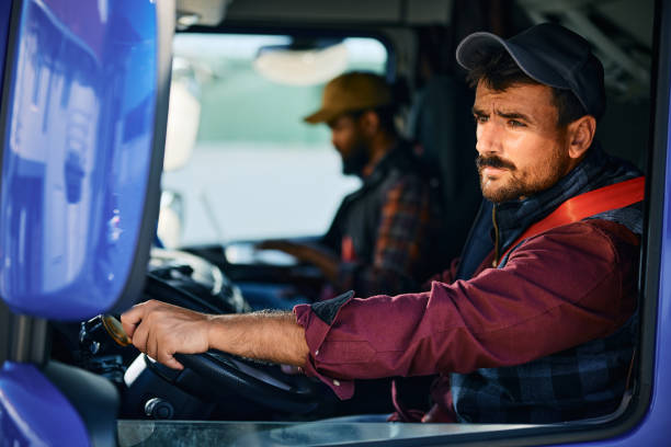 istock Professional truck driver driving in reverse while looking in side view mirror. 1904502121
