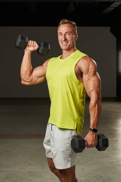 istock a handsome Caucasian athlete with pumped up arms and shoulders holds two large heavy dumbbells in his hands. Raises one hand up and smiles 1904520314