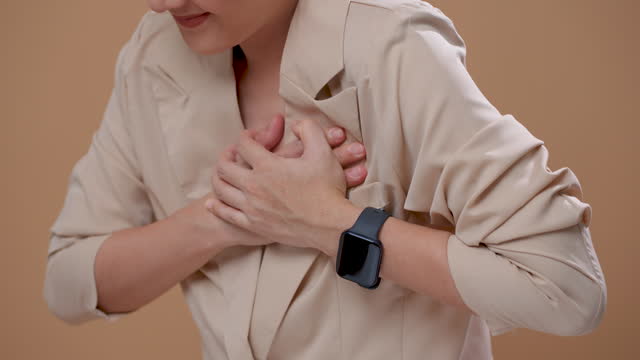 Close-up shot of woman suffering from chest pain standing isolated on beige background.