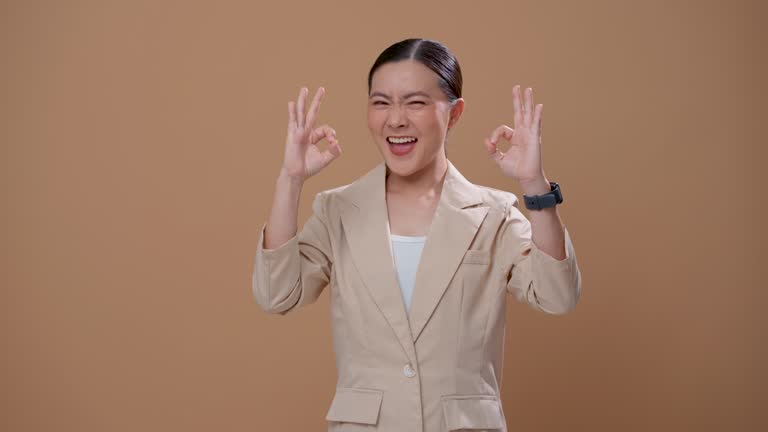 Asian woman happy confident showing OK sign by hand standing isolated over beige background.