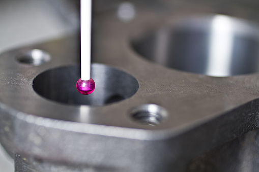 CMM Programming Precision measurement in an industrial setting. A sleek, magenta-tipped probe inspects a metallic component with bolt holes for mechanical assembly. Fort Wayne, Indiana.