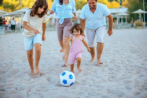 Family is playing soccer on the beach