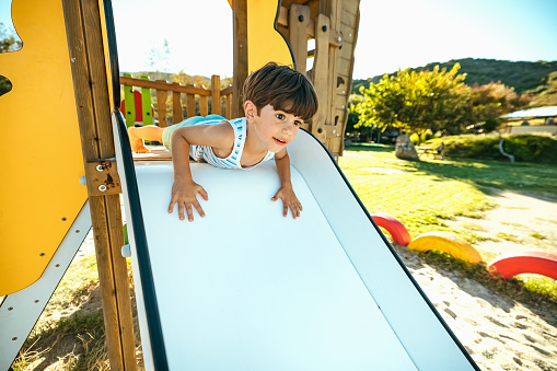 Boy goes down a slide on a beach playground