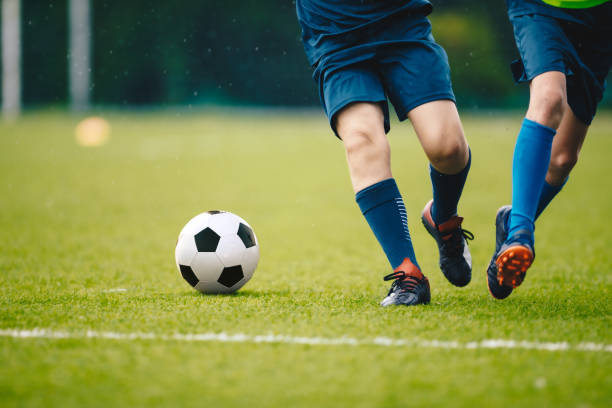 dos jugadores de fútbol adultos corriendo y pateando una pelota de fútbol. piernas de dos jóvenes futbolistas en un partido. las piernas de los jugadores juveniles del fútbol europeo en acción - soccer ball youth soccer event soccer fotografías e imágenes de stock