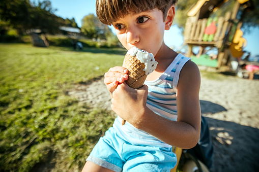 Boy eating an ice cream standing near seafront. Little boy on vacation treating himself to an ice cream.