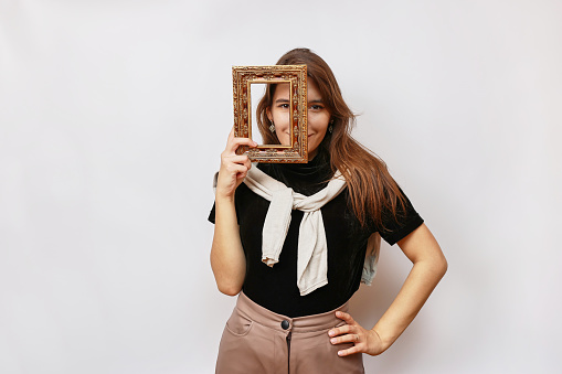 A beautiful girl poses for the camera, looking into a photo frame.