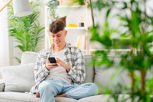 Selective focus on a young man sitting on the sofa using phone