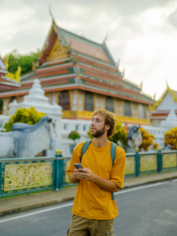 Cheerful man using smartphone during field trip to temples in Bangkok on his vacation to Thailand