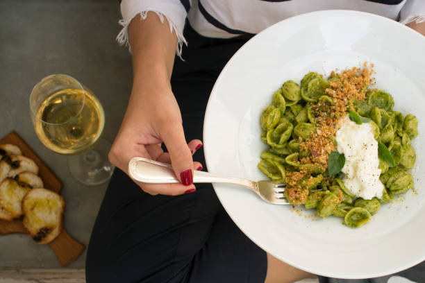 người phụ nữ với móng tay màu đỏ, cầm một cái nĩa và đĩa với mì ống xanh, trong nền rượu vang trắng trong một chiếc cốc thủy tinh và một tấm gỗ với bruschetta - massa tuscany hình ảnh sẵn có, bức ảnh & hình ảnh trả phí bản quyền một lần