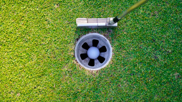 istock white golf ball in hole on green grass good for background with sunlight. 1904675328