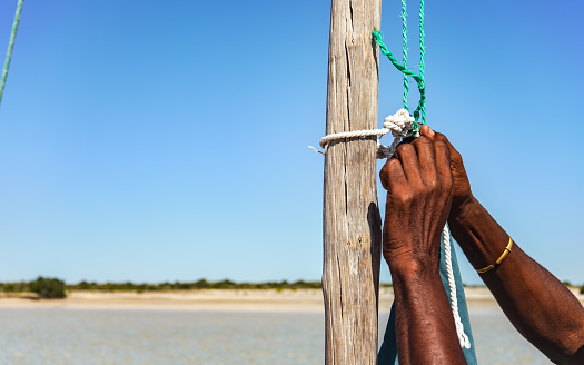 Local Malagasy man securing sail rope to a wooden pole of his ship, detail to hands only