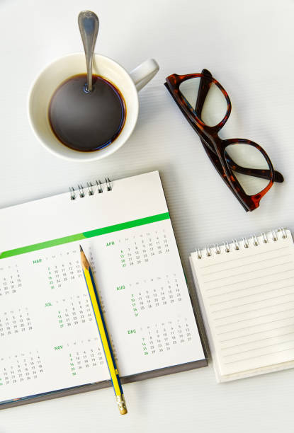 Desk calendar 12 months year 2025 with notepad eyeglasses pencil and hot coffee, object background