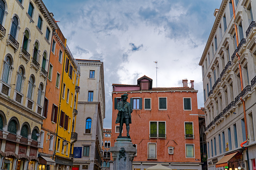 Looking up to green metal stature of Carlo Goldoni. Staute made by Italian artist Antonio Dal Zotto in the year of 1883 and located at town square named Bartolomeo Square at Italian City of Venice.. Photo taken August 6th, 2023, Venice, Italy.