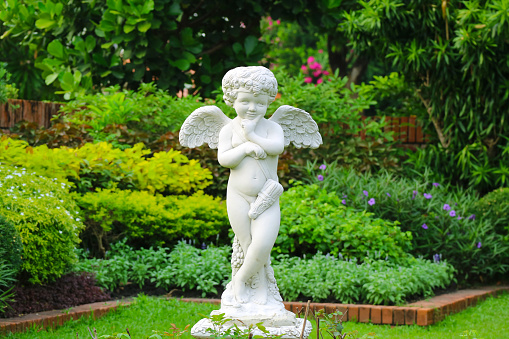 Adorable naughty cupid sculpture in a  freshly green garden