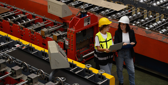 Top view of industrial executive and factory worker wearing hard hat working in metal engineering industry. Overhead view of teamwork in uniforms, hard hats and computers standing on the factory floor