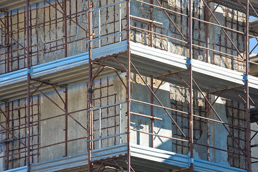 Restoration of a damaged reinforced concrete structure - weathered reinforced concrete structure with damaged and rusty metallic reinforcement  and metal scaffolding on a construction site