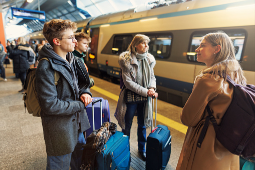 Family off-season winter city break. Mother and three teenagers are standing at the railroad station, next to a train. They are waiting to embark the train.
Shot with Canon R5