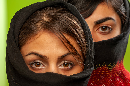 close up of two young women in veil looking at the camera at green background