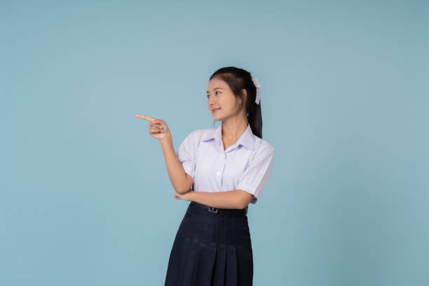 istock Asian female high school student pointing and looking Used for displaying websites or posters. Educational presenter of Institutes and tutoring schools Taking photos in a studio with a blue background 1904825124