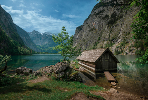 Boathouse with mountain cliffs on lake Obersee at Berchtesgaden Bavaria, clouds in blue sky, turquoise calm water, Berchtesgaden Bavaria
