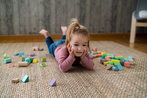 Portrait of a cute little girl lying on the floor whit her toys at home