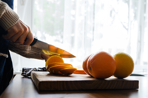 A woman cuts oranges with a knife on a board. White copy space in the background for your text