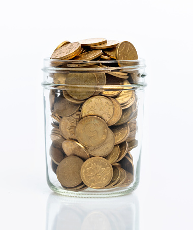 Glass jar full of coins on white background.