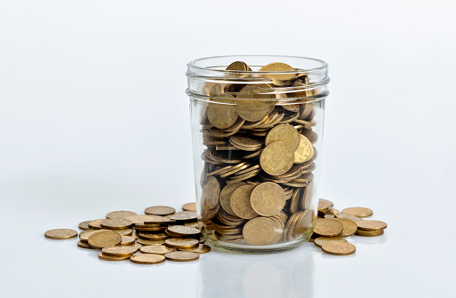 Coins spilling out of a glass jar on white background.
