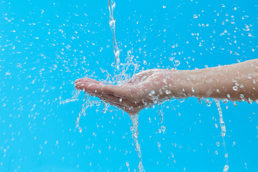 Close up of woman hand under flowing water on blue background.