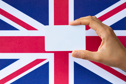 Hand holding blank card in front of flag of United Kingdom. Representing identity and citizenship concept.