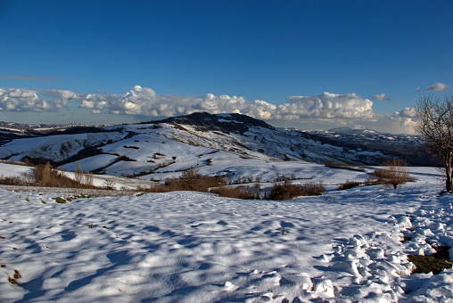view of the snow-capped hills of Montefeltro in winter against partly cloudy sky
