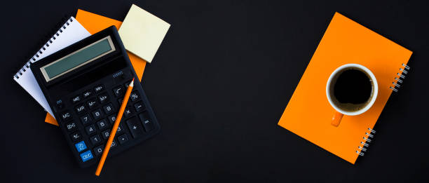 istock Top view of calculator, pencil, notebook and coffee cup on the black background. Copy space. 1904953697