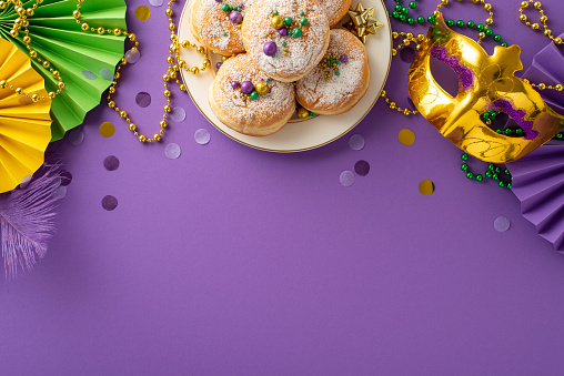 Carnival Delight calorie-free feast. Top-down shot of plate adorned with scrumptious cupcakes, opulent masquerade mask, classic bead necklaces, confetti on purple backdrop with space for text or promo