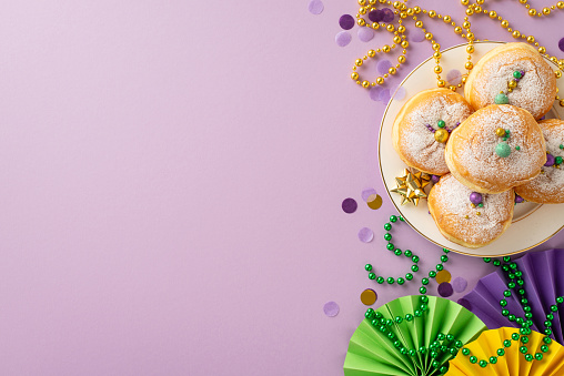 Mirthful Celebration composition. Top view of jubilant table adorned with donuts, decorative fans, ribbon star, confetti, and bead garlands against lively purple backdrop with space for text or ads