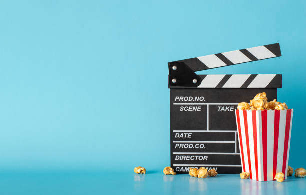 istock Dive into cinematic excitement with much-awaited movie premiere scene. Side view table features clapper, popcorn box against light blue wall, offering perfect spot for text or film advertisements 1904963113