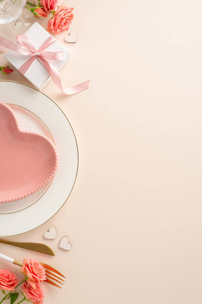 istock Romantic Anniversary Dinner: Overhead vertical shot of beautifully set table with heart-shaped plate, silverware, roses, and themed decor on a soft pastel background. Perfect for sharing love 1904963407