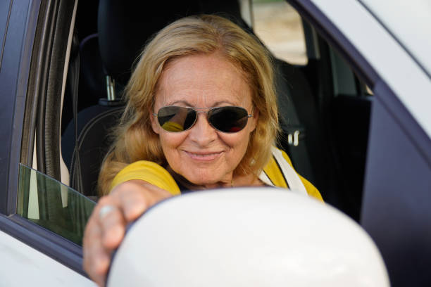 車のバックミラーを調整する成熟した女性 - owner women car rear view mirror ストックフォトと画像