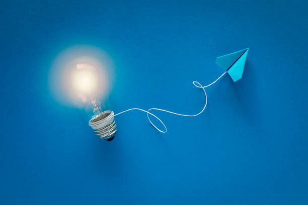 Innovation Bright light bulb attached to a flying blue paper plane with a string on blue background. potential energy stock pictures, royalty-free photos & images