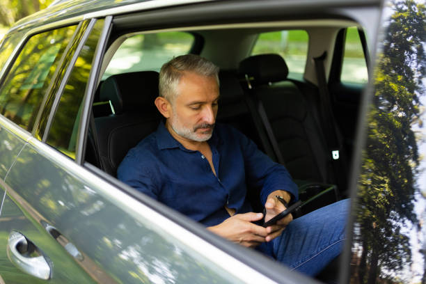 istock Handsome man in suit is using a smart phone and smiling while sitting on back seat in the car 1905010301