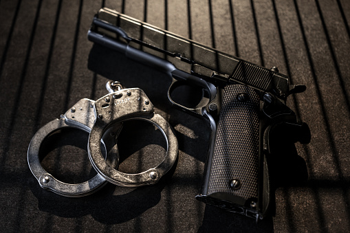 handcuffs, a judge hammer, a gun on a wooden background. criminal offense