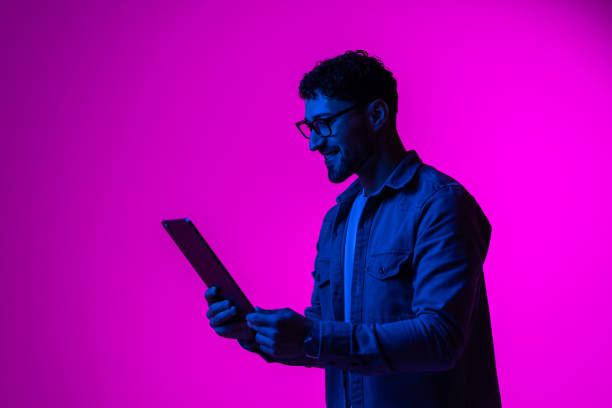istock Cheerful man using modern digital tablet playing video game, watching video content online in neon light 1905030760