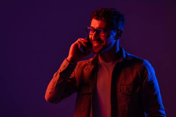 istock Man with phone in hand talking on smartphone, portrait dark blue background, neon light 1905032353