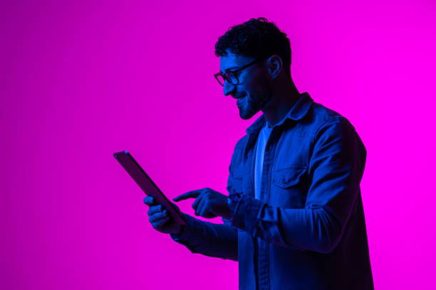istock Cheerful man using modern digital tablet playing video game, watching video content online in neon light 1905038022