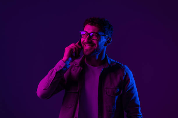 istock Man with phone online video call and selfies on purple background, mixed neon light 1905050942