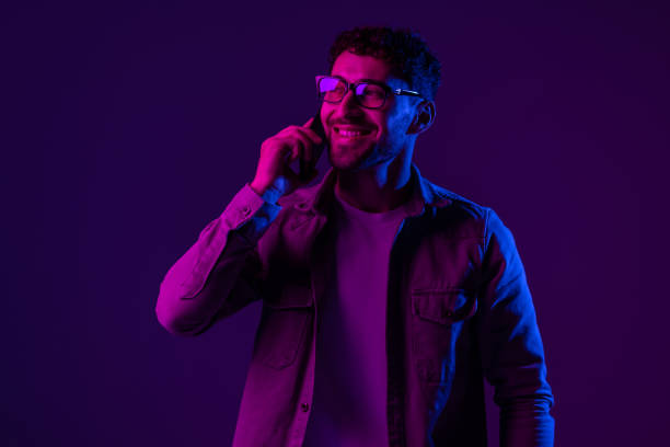 istock Man with phone online video call and selfies on purple background, mixed neon light 1905051990