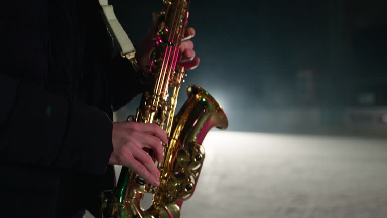 Slowmotion of saxophone player playing a song on a snow covered winter stadium with ice skaters in background