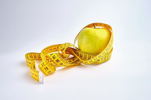 Apple with tape measure on a colored background. Calorie counting and weight loss. Healthy eating concept - calculating daily food intake